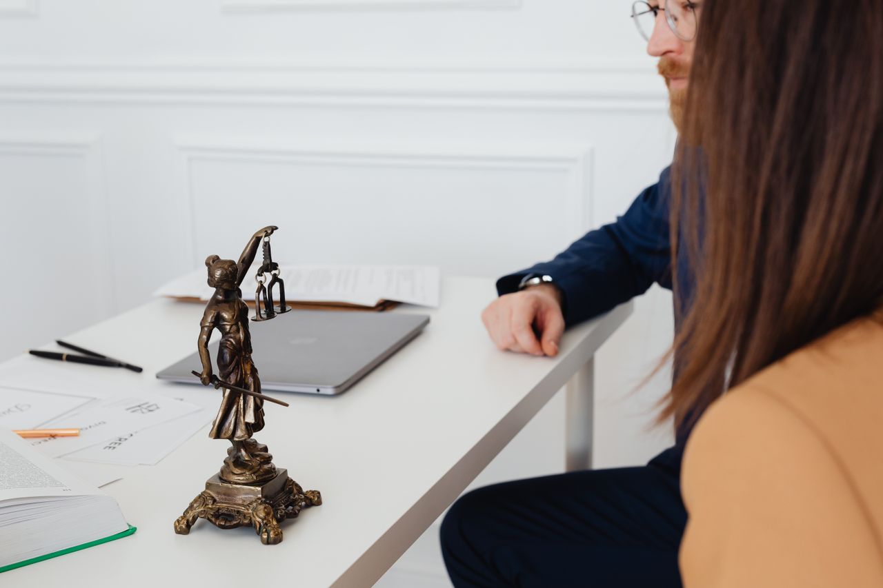 services-02 Professional setting with lawyers and Lady Justice statue discussing legal documents.