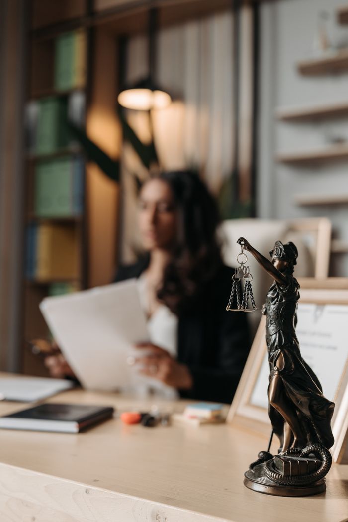 services-01 Close-up of a justice figurine on desk with blurred female lawyer in office setting.